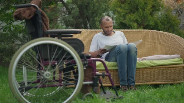 Disabled African American Business Analyst Examining Paperwork Outdoors in Spring Garden