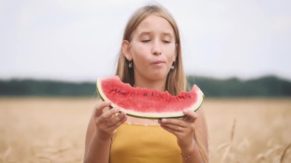 Cute Girl Eating Juicy Watermelon Standing in Wheat Field on Sunny Summer Day