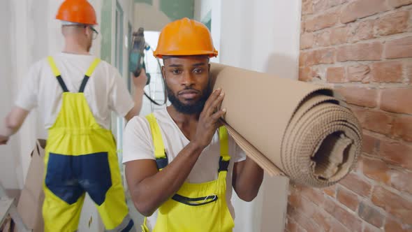 Portrait of African Builder in Safety Helmet Carrying Roll of Construction Material Indoors