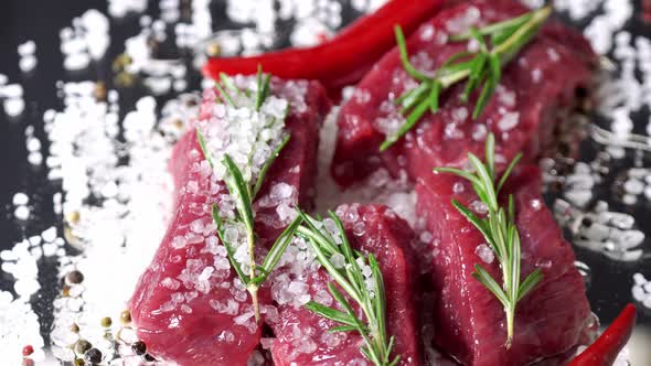 Raw organic beef meat with rosemary spinning on dark background