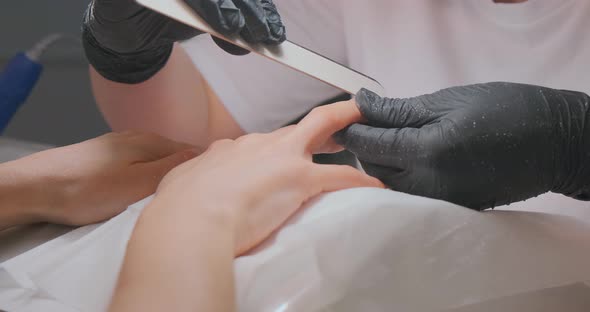 Beautician Polishes Client Nails with File at Table in Salon