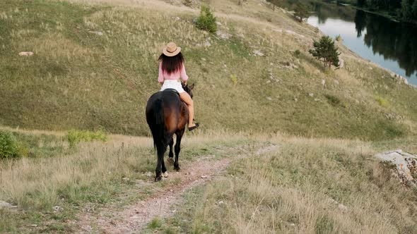 Beautiful Girl in Hat Riding a Horse Among the Hills. Female Rider Rides a Graceful Horse. Horseback