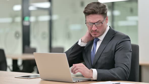 Tired Middle Aged Businessman with Laptop Having Neck Pain in Office 