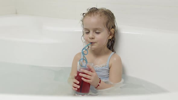 Cute Blonde Girl Takes a Bath in Swimwear and Drinking a Cocktail. Little Child