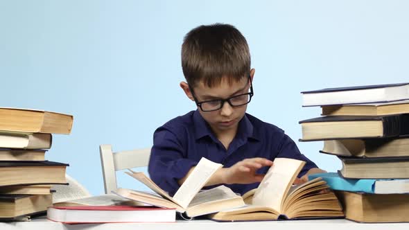 Boy Sits at the Table and Excitedly Leafing Through the Pages of Books. Blue Background.