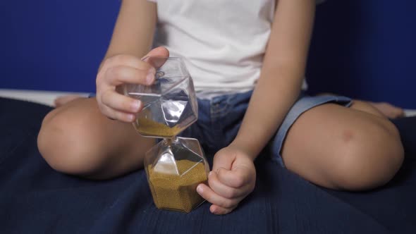 Boy Child is Sitting on a Bed Against a Blue Wall with an Hourglass