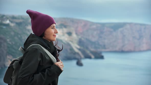 Pleasant Hipster Woman Travel Backpacker Standing High Cliff Peak at Windy Weather Enjoying Nature