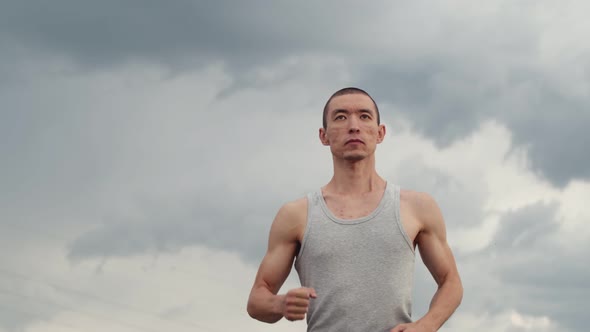 Male runner with athletic build runs along the road against background of an overcast sky, down view