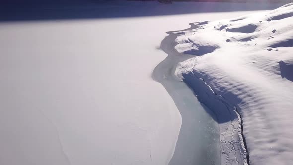 Close aerial view over the shore of a frozen mountain lake to a huge panorama in a valley in Klöntal