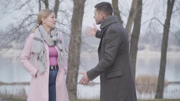 Older Caucasian Woman and Younger Man Arguing in City Park. Irritated Couple with Age Gap