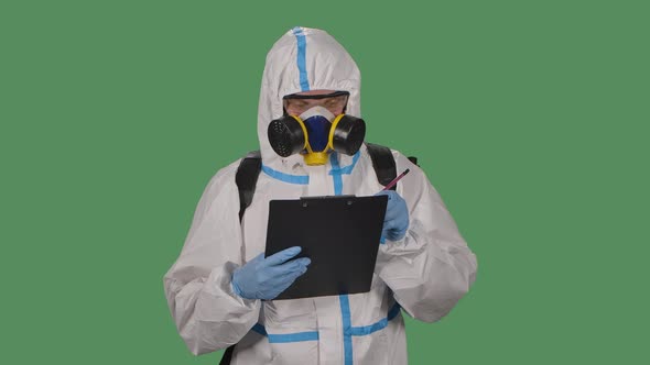 Portrait of a Man in a Protective Suit, Goggles, Gloves and a Respirator Holds a Folder and Marks