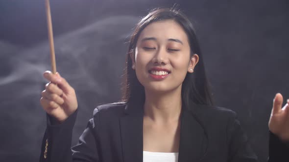 Asian Conductor Woman Holding A Baton And Showing Gesture Quickly In The Black Studio With Fog