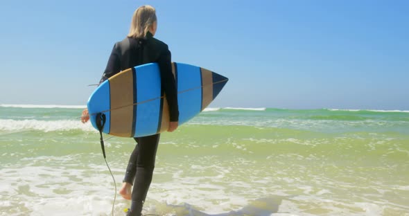 Rear view of active senior Caucasian female surfer running on sea in the sunshine 4k