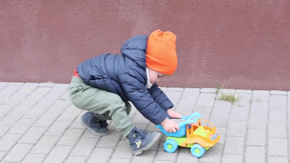 Little Kid Boy Plays with Toy Track Outside Spring Autumn Day Multicolored