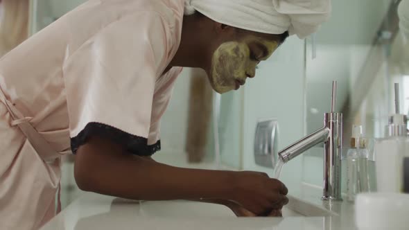 African american attractive woman washing off face mask in bathroom