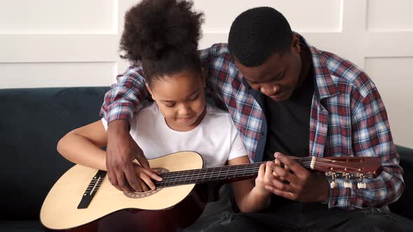 AfricanAmerican Man Teaching His Little Daughter to Play Guitar at Home