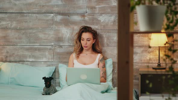 Beautiful Young Woman in Pajamas Working on Laptop