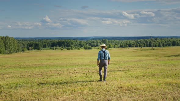 Farmer Wearing Straw Hat Suspenders and Rubber Boots Walking in Mown Field