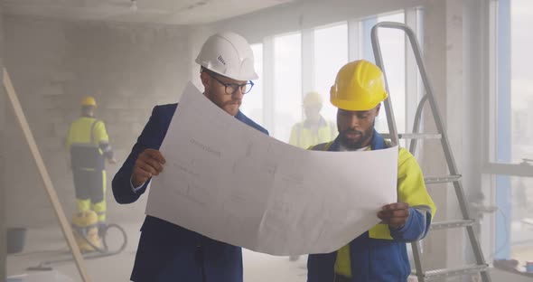 Young Engineer Discussing Blueprint with Building Worker on Construction Site