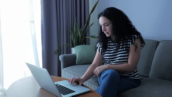 Young Serious Woman Working on Laptop, Sitting on Sofa at Home, Businesswoman Sits at Home Works