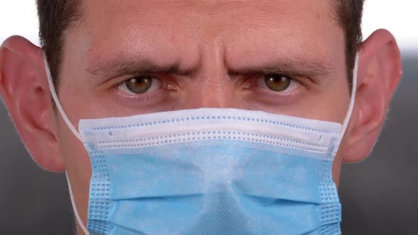 Young Man in a Medical Protective Face Mask Looking at the Camera on the Street Background
