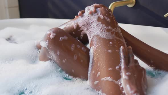 African american woman taking bath and touching her legs in bathroom