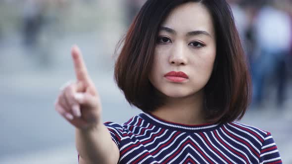 beautiful serious asian Woman says No with Finger in the city street