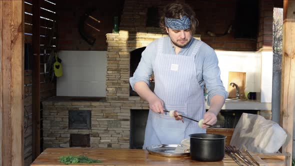 A Man in an Apron Strings Pieces of Meat on a Skewer and Makes a Kebab From It Near the Fireplace