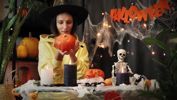 Woman in witch hat painting pumpkin for Halloween.