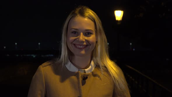 A Young Beautiful Woman Smiles at the Camera in an Urban Area at Night