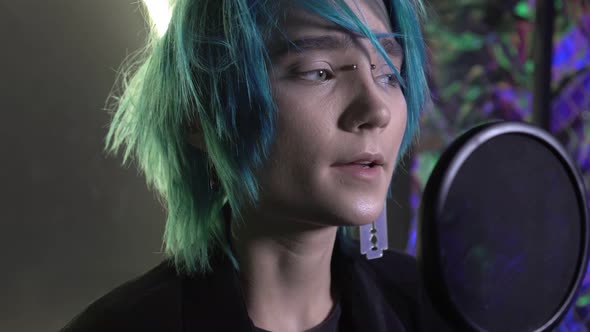 Young Attractive Man with Blue Hair Sings Into a Microphone in a Recording Studio