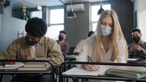 Diverse Students in Medical Mask Sit in Classroom at Lesson Concentrated Listen to Lecture Writing