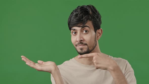 Indian Young Handsome Man Stands on Green Background Holds Copy Space on Hand Points at Empty Place