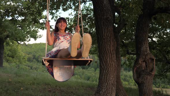 Child Swinging on a Swing in Park in Sun. Young Girl Swinging on Rope Swing on an Oak Branch. Teen