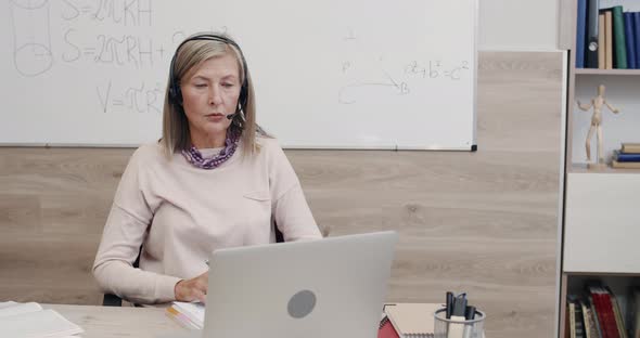 Crop View of Positive Female Professor in Wireless Headset with Mic Talking While Looking at Laptop