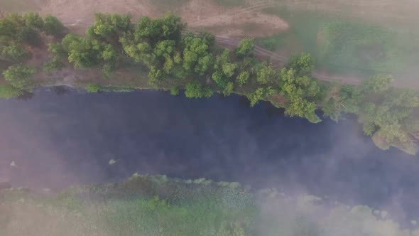 Top-down View Over Little Misty River Streaming Through Valley. Aerial Shot of Beautiful Foggy