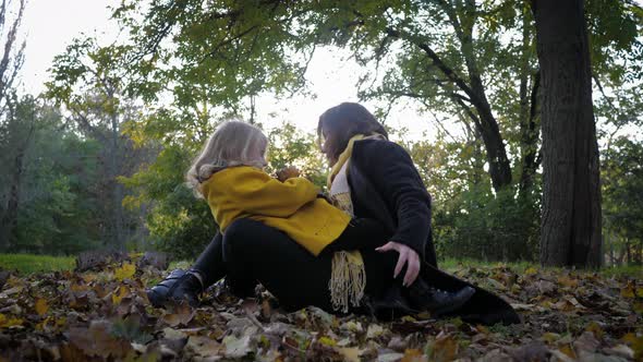 Motherly Care, Young Mother Hugs Her Beloved Joyful Daughter Tightly While Sitting on Lawn Covered