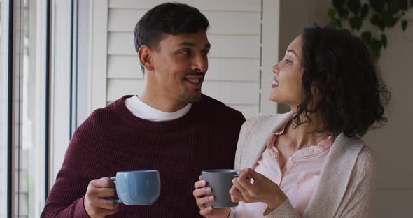 Romantic hispanic couple embracing standing in window having coffee