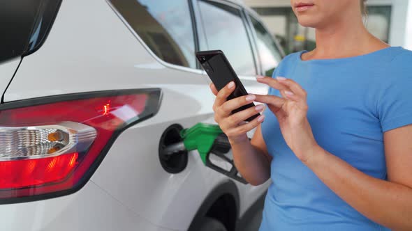 Woman Using Smartphone While Her Car Is Refueling