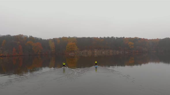 Man and Woman on Sup Paddle Boards at Wide River with Small Island on Golden Autumn Forest