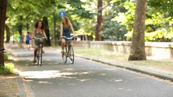 Couple of female friends riding bikes on the street at park on a sunny day