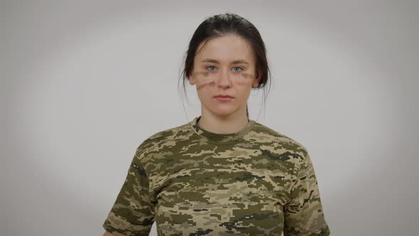 Serious Young Military Woman Applying Camo Face Paint Looking at Camera