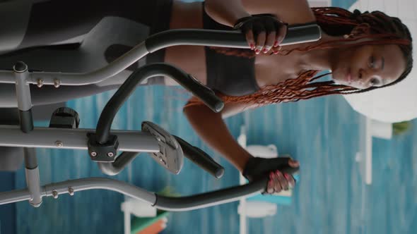 Verical Video Fit Athletic Black Woman Running on Elliptical Bike Watching Wellness Routine