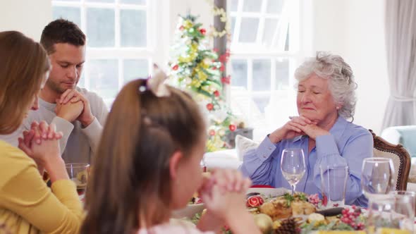 Caucasian family sitting on dining table praying together before lunch