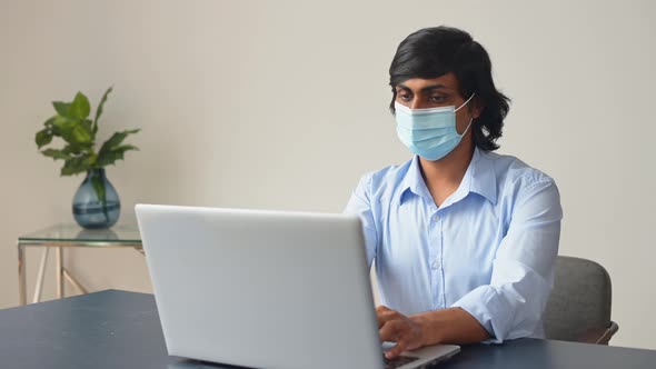 Portrait of Focused Young Indian Man Wearing Surgical Medical Mask Using Laptop