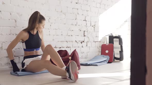 During a Break in Kickboxing Training, a Young Pretty Girl Sits Next To a Wall and Drinks Water.