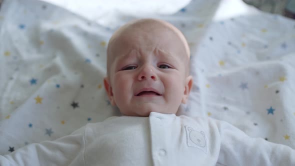 Funny Baby Lies in Bed Looks at the Camera and Wants to Cry