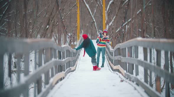 Two Young Women Friends in Colorful Sweaters Taking Photos on the Bridge