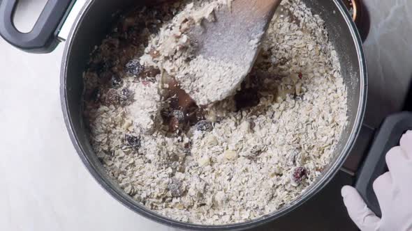 Bird's eye view of woman wearing latex single use gloves, stirring home-made energy bars mixture, us