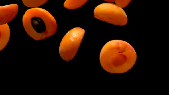 Fresh Juicy Apricot Halves are Flying Diagonally on a Black Background